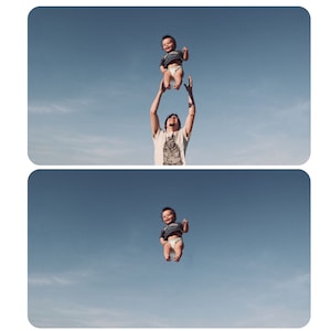 May include: A man is holding a baby up in the air against a blue sky with white clouds. The baby is wearing a diaper and a blue shirt. The man is wearing a white shirt and has brown hair.