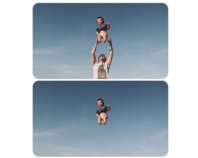 May include: A man is holding a baby up in the air against a blue sky with white clouds. The baby is wearing a diaper and a blue shirt. The man is wearing a white shirt and has brown hair.