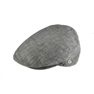 Pode incluir: Boné cinza estilo newsboy feito de tecido texturizado. O boné tem uma coroa arredondada e uma aba curta e rígida. Um pequeno emblema prateado está na lateral.