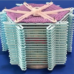 Può includere: Un telaio per la maglia esagonale con un pezzo di maglia viola in cima e una pila di 20 telai in plastica blu chiaro sotto. Il telaio superiore ha il numero "6" stampato su di esso.