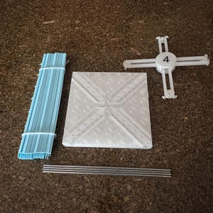 May include: An assortment of disassembled white and blue event decorations. The components include a stack of blue plastic pieces, a square white base, a white cross-shaped piece with the number 4, and several silver rods. The items are arranged on a brown surface.