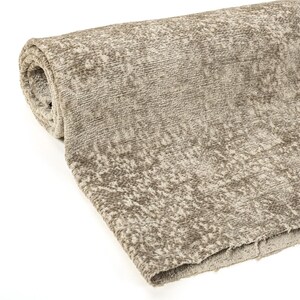 May include: A rolled-up section of textured fabric in shades of beige and brown. The material has a soft, plush appearance with a subtle pattern. The edges of the fabric are visible, showing the layers of the roll. This textile is suitable for upholstery or home decor.