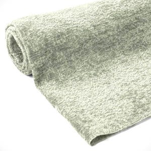May include: A rolled-up, light green fabric with a textured, plush surface. The fabric has a soft, velvety appearance and a subtle sheen. The material appears to be a heavy weight, suitable for upholstery or drapery.