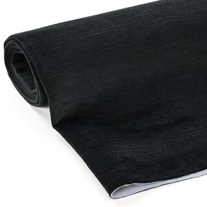 May include: A rolled-up length of black corduroy fabric. The fabric has a ribbed texture and a soft, velvety appearance. The roll is partially unraveled, revealing the white backing of the material. The corduroy is a solid, dark black color.