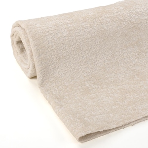 May include: A rolled-up, beige-colored fabric with a textured surface. The fabric appears soft and plush, with a subtle, light-colored hue. The roll is partially visible, showcasing the fabric's thickness and texture. The material is likely used for home decor.