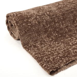 May include: Rolled-up brown fabric with a textured, speckled pattern. The fabric appears soft and plush, with a slight sheen. The color is a warm, earthy tone, suitable for home decor or textile projects.