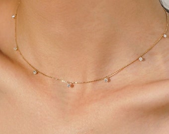 May include: A delicate gold chain necklace with small, clear diamonds dangling from it. The necklace is worn by a person, but the focus is on the necklace itself.