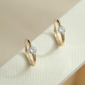 May include: A pair of gold hoop earrings with a single clear cubic zirconia stone on each hoop.