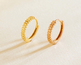 May include: A pair of small gold and rose gold hoop earrings with a textured design. The earrings are simple and elegant.