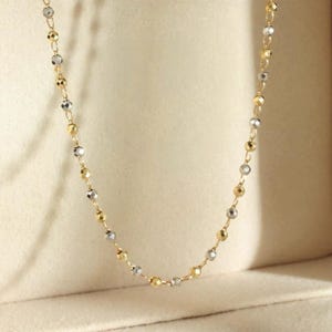 Peut inclure: Un collier délicat avec des perles alternées dorées et argentées. Les perles sont espacées régulièrement le long d'une fine chaîne, créant un éclat subtil. Le collier est présenté sur un fond neutre, soulignant son design élégant. Idéal pour un usage quotidien ou des occasions spéciales.