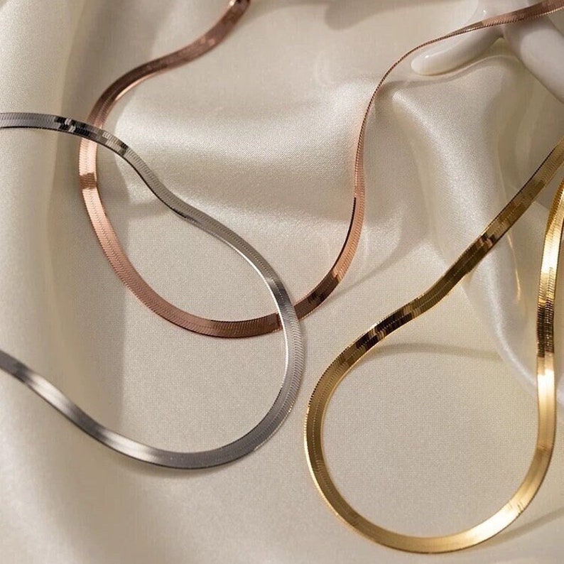 Puede incluir: Tres collares de cadena de serpiente de oro, plata y oro rosa sobre un fondo de sat&eacute;n blanco.