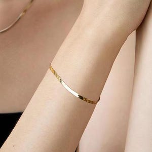 May include: A thin gold bracelet with a slightly curved design.