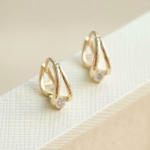 Könnte beinhalten: Ein Paar goldene Creolen mit einem kleinen, klaren Stein in der Mitte jedes Creolen.