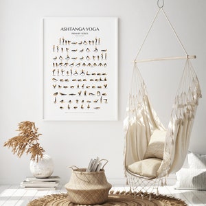 May include: A white poster with the text "Ashtanga Yoga Primary Series" and a series of black and gold illustrations of yoga poses. The poster is hanging on a white wall in a room with a white hammock chair, a woven basket, and a rug.