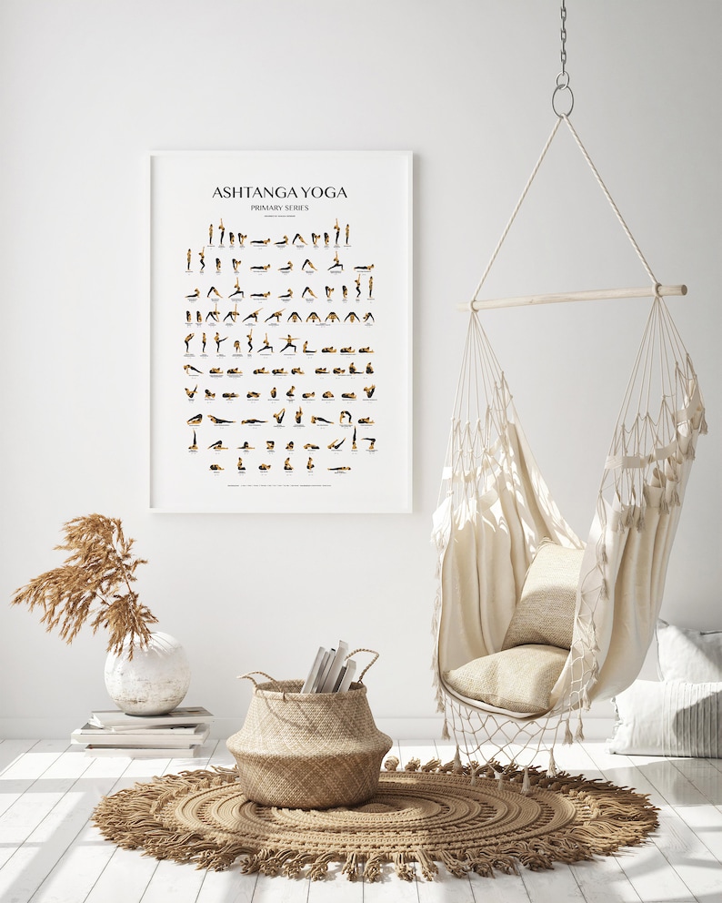May include: A white poster with the text "Ashtanga Yoga Primary Series" and a series of black and gold illustrations of yoga poses. The poster is hanging on a white wall in a room with a white hammock chair, a woven basket, and a rug.