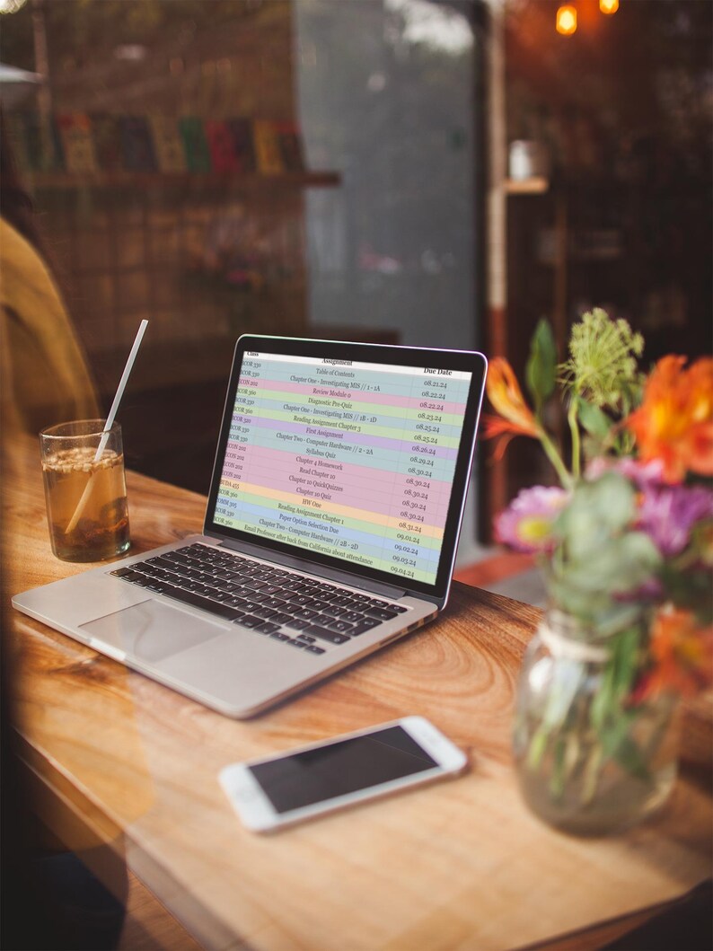 May include: A laptop computer with a bright, colorful spreadsheet open on the screen. The spreadsheet lists various assignments and due dates. The laptop is on a wooden table with a glass of iced tea and a smartphone.