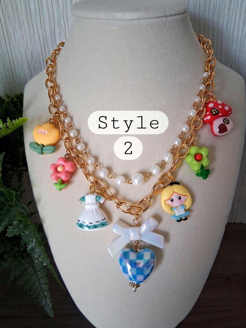 Pu&ograve; includere: Collana a catena color oro con ciondoli multipli, tra cui un fungo, un fiore, un vestito, un cuore e un personaggio di Alice nel Paese delle Meraviglie. La collana ha una fila di perle e il testo "Style 2".