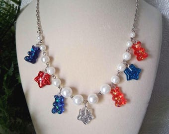 May include: A silver chain necklace with white faux pearls and colorful charms. The charms include red and blue glittery stars and gummy bear shapes. A silver charm hangs in the center.