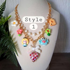 Pu&ograve; includere: Una collana dorata con vari ciondoli, tra cui fiori, una teiera e un ciondolo a forma di cuore. La collana presenta una catena di perle e una catena. Il testo "Style 1" &egrave; visibile nell'immagine.