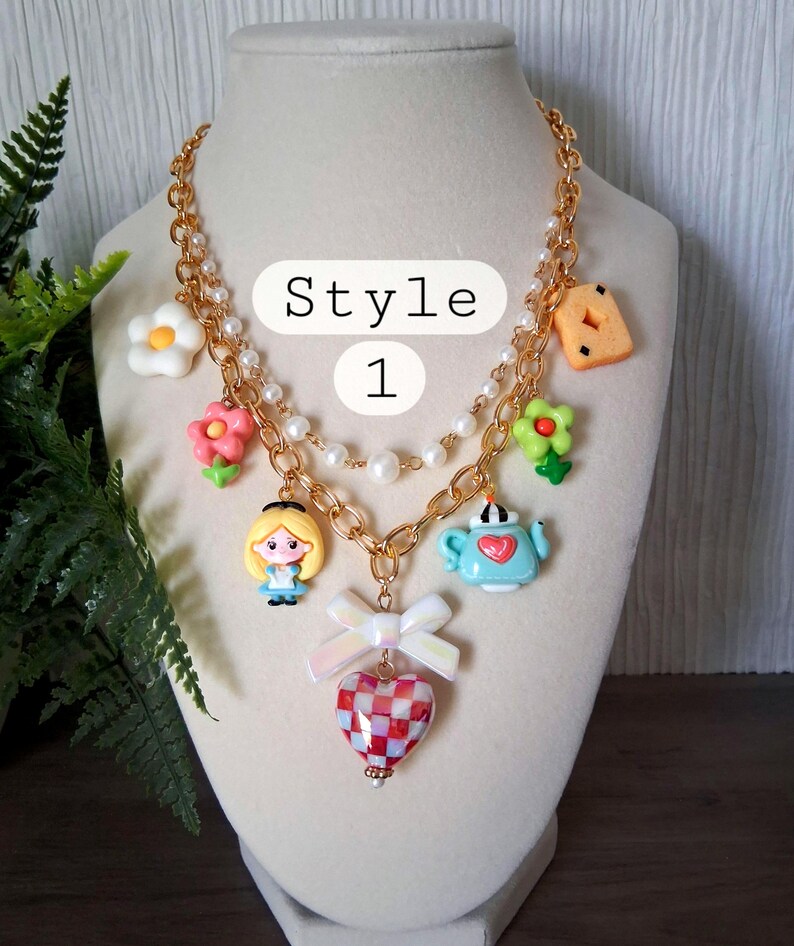 Pu&ograve; includere: Una collana dorata con vari ciondoli, tra cui fiori, una teiera e un ciondolo a forma di cuore. La collana presenta una catena di perle e una catena. Il testo "Style 1" &egrave; visibile nell'immagine.
