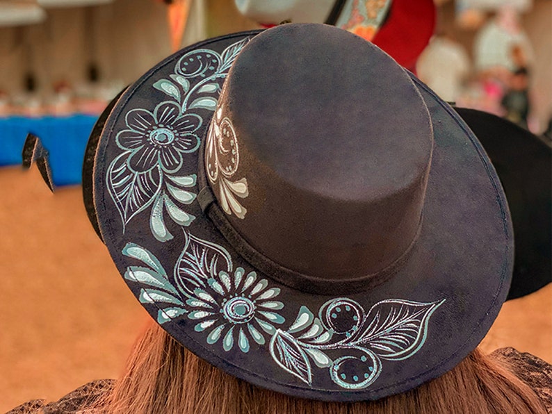 May include: A black felt fedora hat with a wide brim, decorated with a silver floral design. The hat has a flat top and a narrow band around the crown.