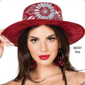 May include: A wide-brimmed hat in red with a white floral design. The hat has a flat top and a wide brim. The hat is made from a soft, suede-like material. The hat is being worn by a person with long brown hair and red lipstick.
