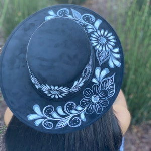 May include: A black felt hat with a wide brim and white floral designs painted on the brim.