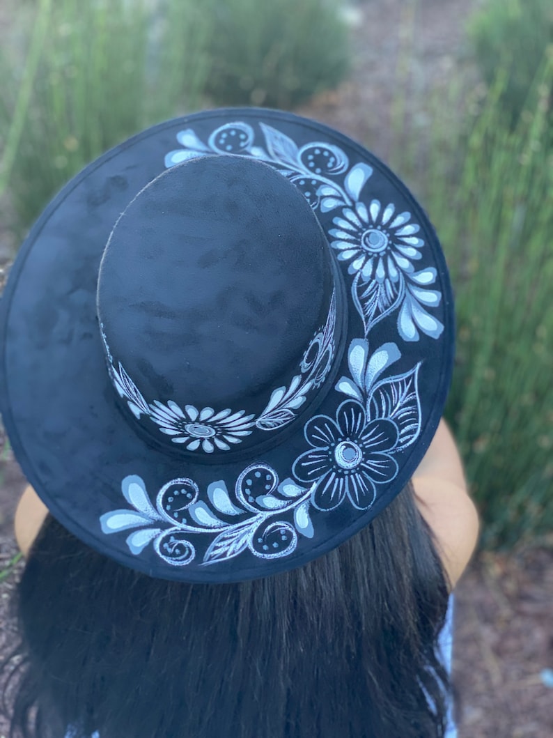 May include: A black felt hat with a wide brim and white floral designs painted on the brim.
