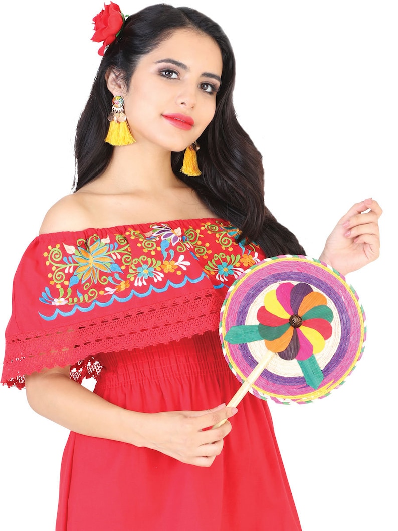 May include: A woman wearing a red off-the-shoulder dress with colorful embroidery and a white lace trim. She is holding a colorful woven fan with a wooden handle.
