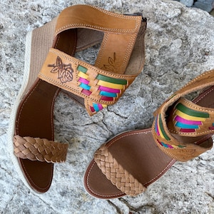 Peut inclure: Une paire de sandales en cuir marron avec des lani&egrave;res tiss&eacute;es et des accents color&eacute;s. Les sandales ont un talon compens&eacute; et un motif floral sur la lani&egrave;re.