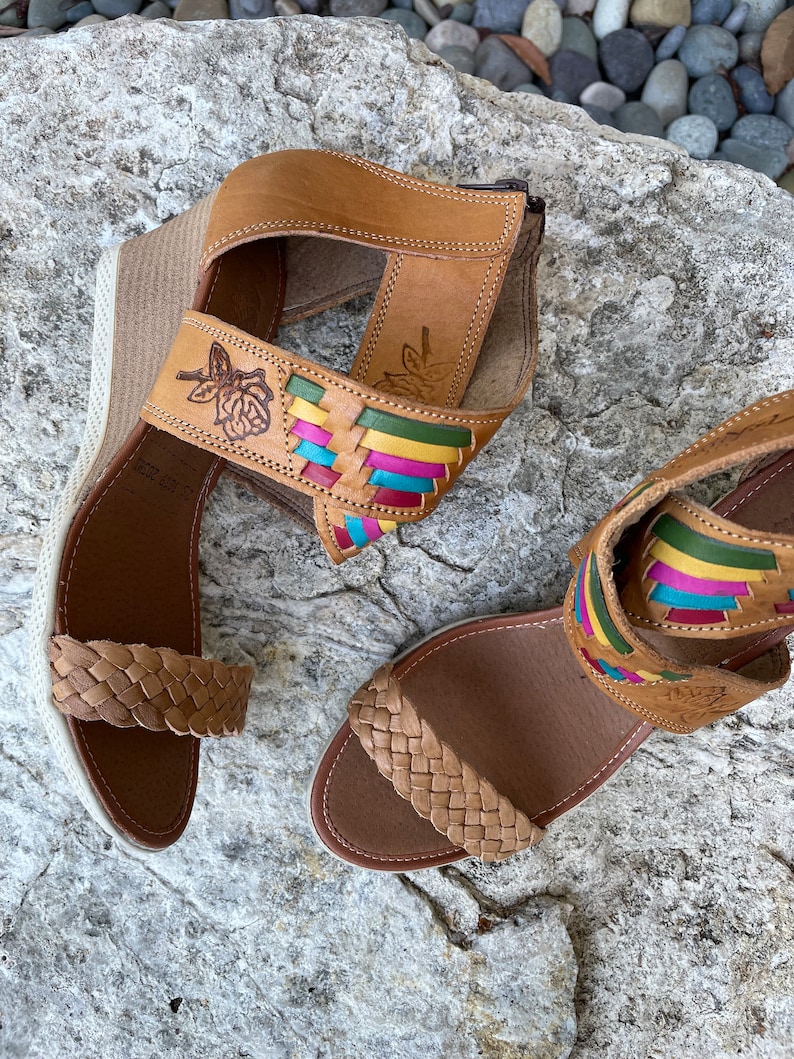 Peut inclure: Une paire de sandales en cuir marron avec des lani&egrave;res tiss&eacute;es et des accents color&eacute;s. Les sandales ont un talon compens&eacute; et un motif floral sur la lani&egrave;re.