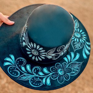 May include: A black hat with a wide brim and a floral design painted in white and blue.