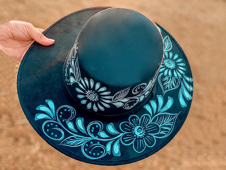May include: A black hat with a wide brim and a floral design painted in white and blue.