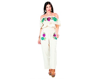 May include: A white off-the-shoulder top and pants set with floral embroidery. The top has a ruffled neckline and the pants have a wide leg.
