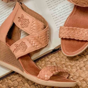 Peut inclure: Une paire de sandales en cuir tiss&eacute; avec un talon compens&eacute;. Les sandales sont de couleur brun clair et ont un motif floral sur les lani&egrave;res. Les sandales sont pos&eacute;es sur un tapis tiss&eacute;.