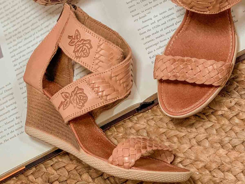 Peut inclure: Une paire de sandales en cuir tiss&eacute; avec un talon compens&eacute;. Les sandales sont de couleur brun clair et ont un motif floral sur les lani&egrave;res. Les sandales sont pos&eacute;es sur un tapis tiss&eacute;.