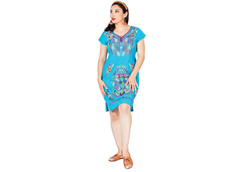 May include: A woman wearing a turquoise blue dress with colorful embroidery. The dress has short sleeves and a V-neckline. The embroidery features floral and geometric patterns.