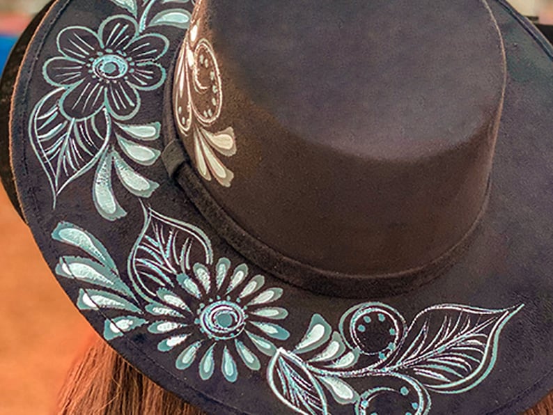 May include: A black fedora hat with a silver and teal floral design painted around the brim.