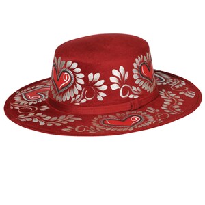 May include: A red felt hat with a wide brim and silver painted floral designs and hearts.