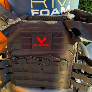 Peut inclure: Gilet tactique noir avec des sangles réglables et un patch logo VALORANT rouge.