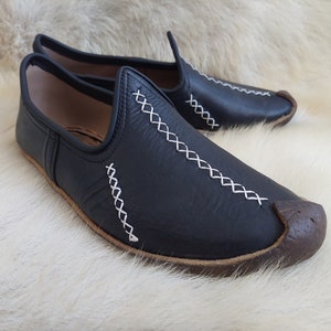 May include: A pair of black leather slippers with white stitching. The slippers have a pointed toe and a flat sole.