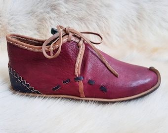 May include: Burgundy leather shoe with a lace-up closure and decorative stitching. The shoe has a pointed toe and a flat sole.