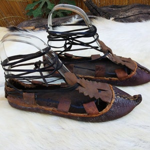 May include: A pair of brown leather sandals with laces. The sandals have a pointed toe and are tied up the ankle with leather laces.