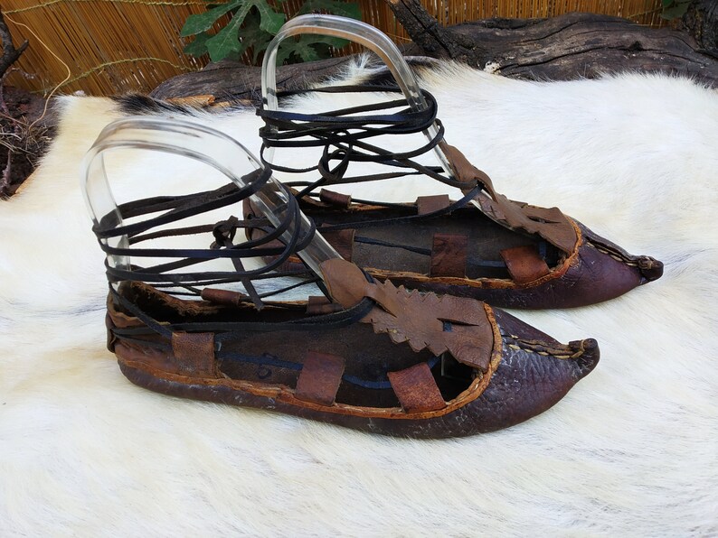 May include: A pair of brown leather sandals with laces. The sandals have a pointed toe and are tied up the ankle with leather laces.
