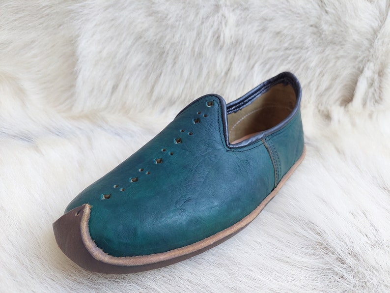 May include: A teal blue leather slipper with a pointed toe and a brown leather trim. The slipper has a decorative pattern of small holes.