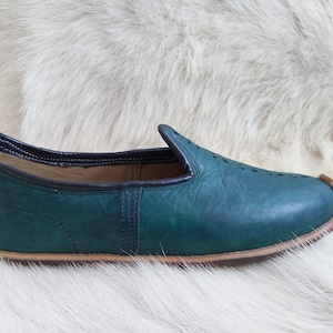 May include: A pair of teal blue leather slippers with a pointed toe and a brown leather sole.