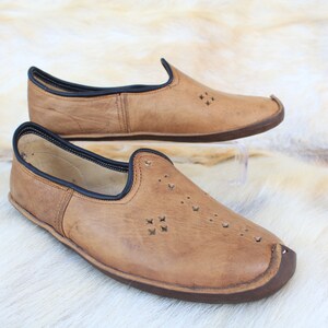Pu&ograve; includere: Un paio di scarpe marroni in pelle da infilare con bordi neri e ritagli decorativi. Le scarpe hanno una punta arrotondata e una suola piatta.