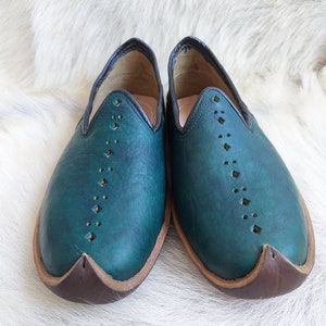 May include: A pair of teal blue leather slippers with a pointed toe and decorative stitching. The slippers have a brown leather sole.