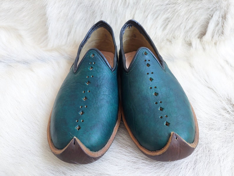 May include: A pair of teal blue leather slippers with a pointed toe and decorative stitching. The slippers have a brown leather sole.
