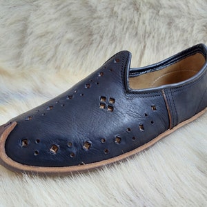 K&ouml;nnte beinhalten: Schwarze Lederschuhe zum Hineinschl&uuml;pfen mit einem dekorativen Ausschnittmuster. Die Schuhe haben eine spitze Zehenpartie und eine braune Ledersohle.